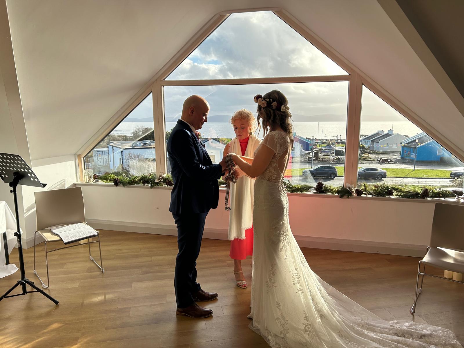 Ring exchange during a wedding ceremony officiated by Edel Garvey, with coastal views behind