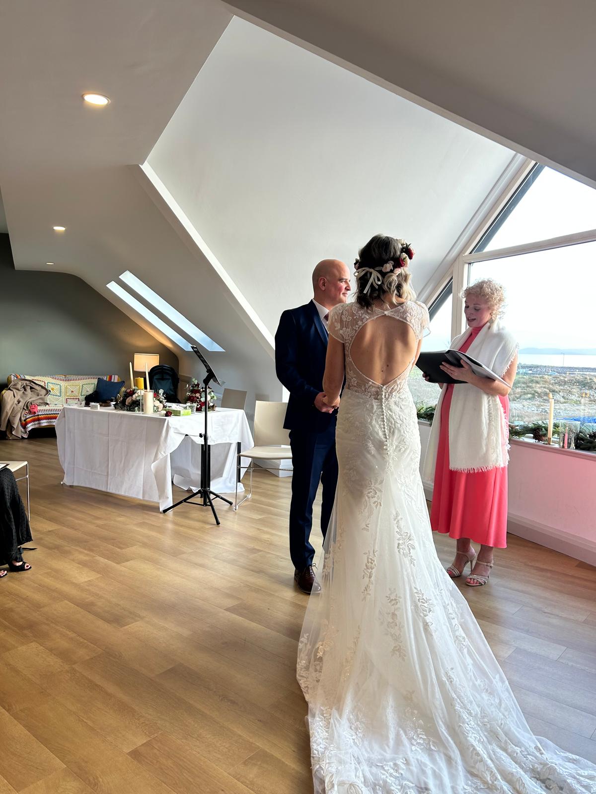 Couple exchanging vows with Edel Garvey officiating, Atlantic coastline visible through the window