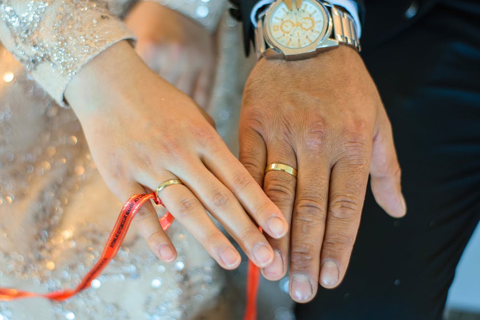 Joined hands of a couple wearing wedding rings, bound with a red ribbon during a handfasting ritual