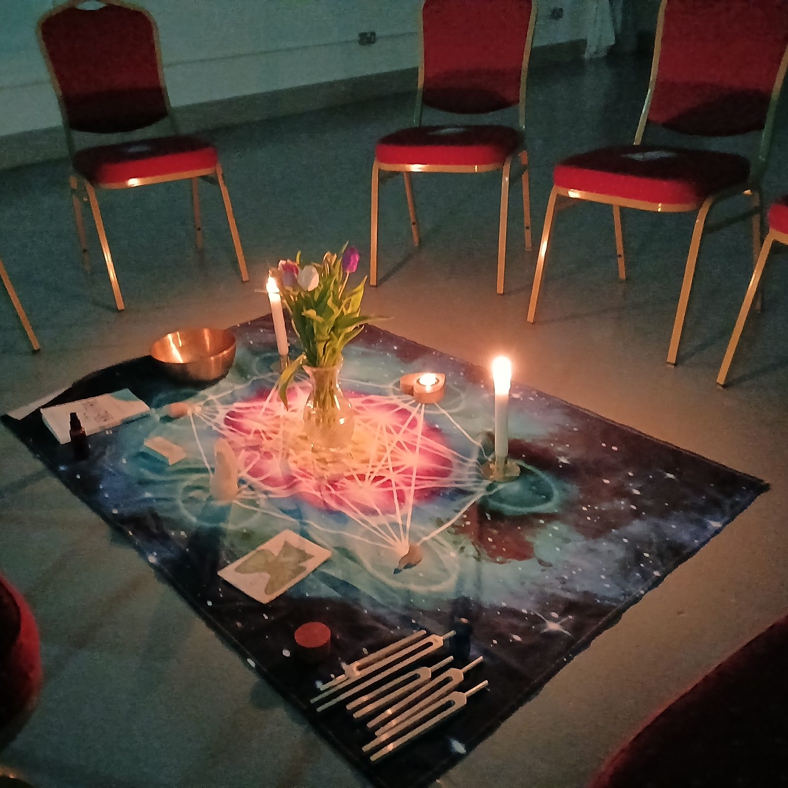 Overhead view of the altar cloth during an evening sound bath — crystal grid glowing in the candlelight with tulips, singing bowl and tuning forks ready