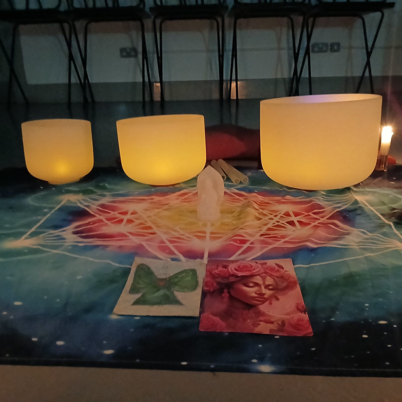 Three crystal singing bowls lit from within during an evening session, oracle cards and lit candle on the sacred geometry cloth