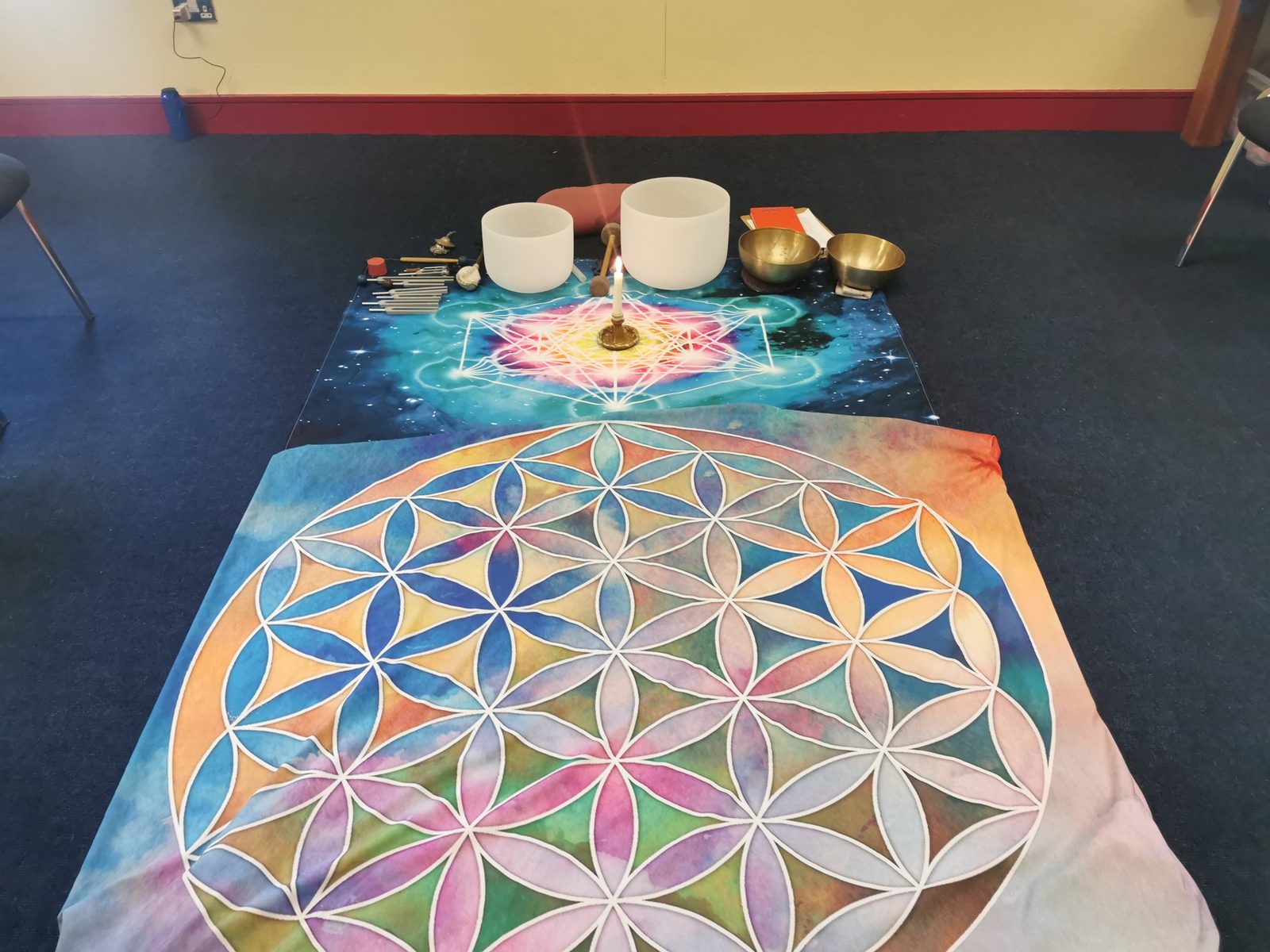 Crystal and brass singing bowls, wand, and a lit candle arranged on a sacred geometry mat — Edel's ceremony setup before a session begins